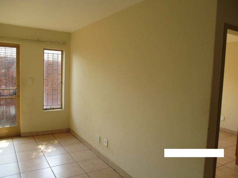 An empty living area featuring tiled flooring, neutral wall finishes, and a glass door leading to an outdoor space with security bars.
