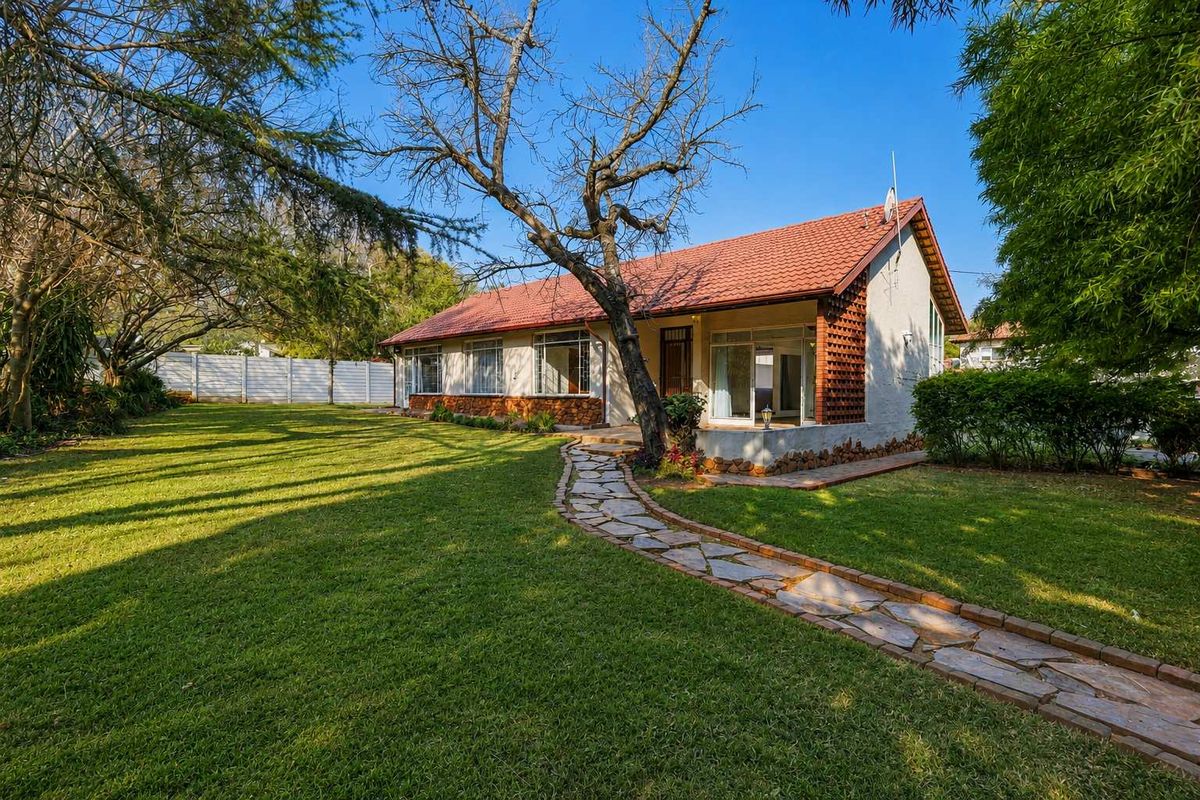 A view of the rear exterior of the house featuring a well-maintained lawn, stone pathway, and traditional tiled roof architecture.