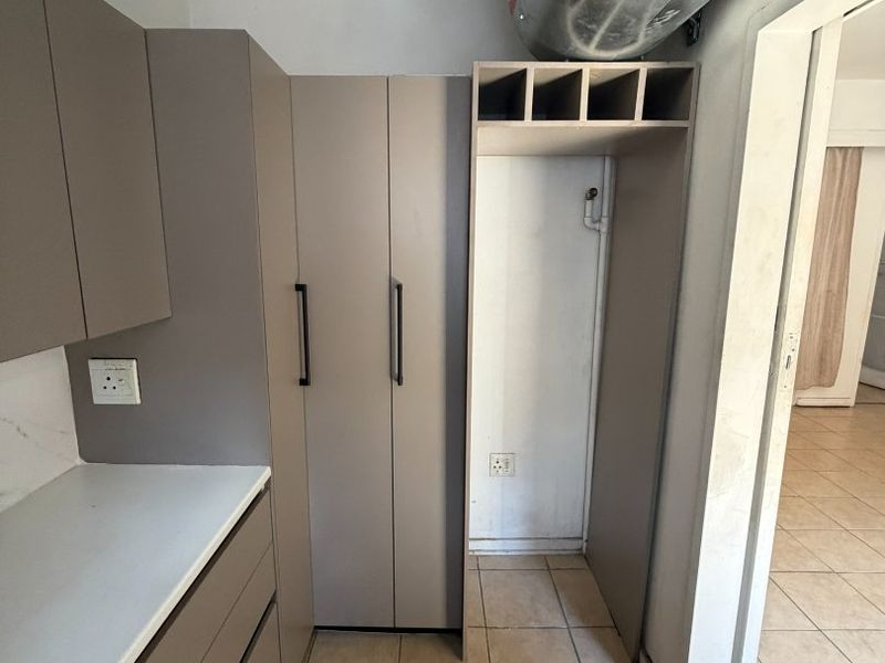 A functional kitchen area featuring modern taupe cabinetry, tiled flooring, and an exposed ventilation duct, offering a blank canvas for further customization.