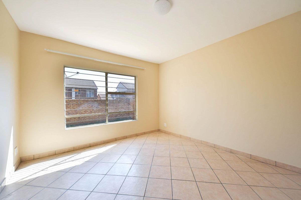 A bright, empty bedroom featuring neutral wall paint, tiled flooring, and a large window with security bars.