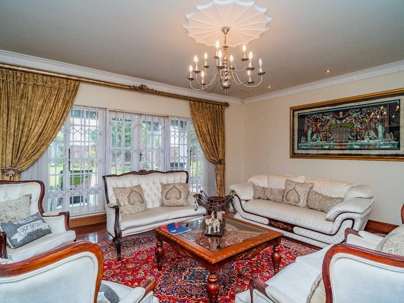 A formal living room featuring hardwood flooring, decorative crown molding, a classic chandelier with a ceiling rose, and security gates over the windows.