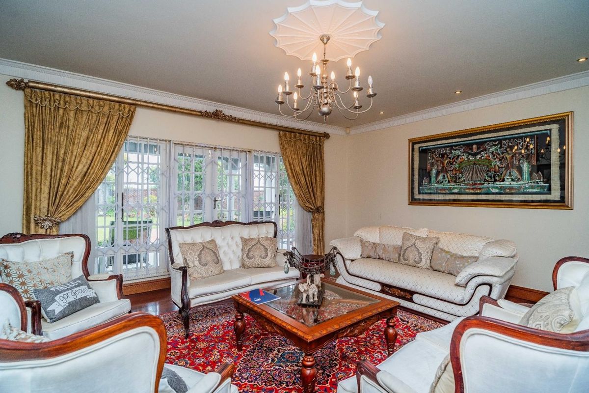 A formal living room featuring hardwood flooring, decorative crown molding, a classic chandelier with a ceiling rose, and security gates over the windows.