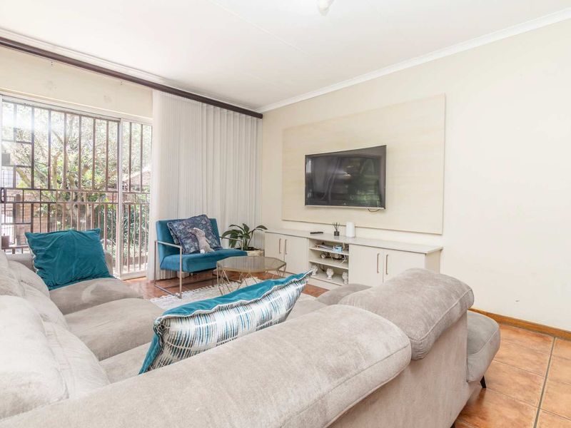 A comfortable living room featuring tiled flooring, a built-in media console, and a sliding glass door with security gate providing access to the outdoors.
