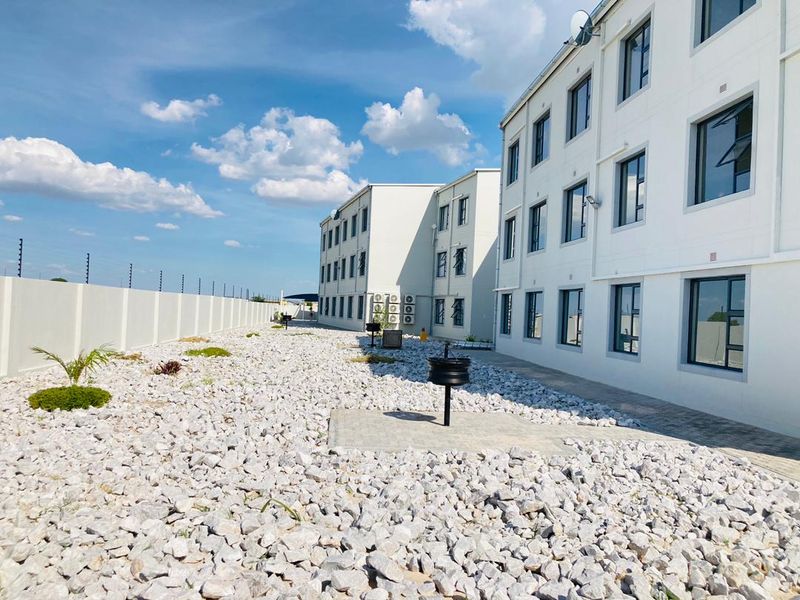 Rear view of the apartment complex featuring a low-maintenance gravel garden, paved walkways, and secure perimeter wall with electric fencing.