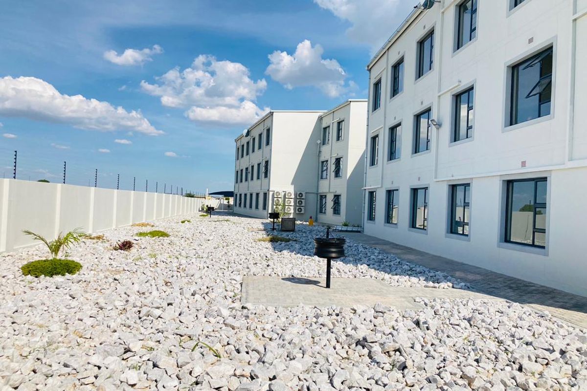 Rear view of the apartment complex featuring a low-maintenance gravel garden, paved walkways, and secure perimeter wall with electric fencing.