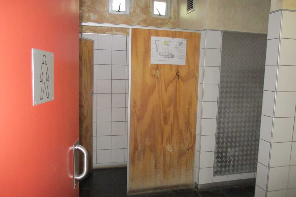 A functional office restroom facility featuring tiled walls, a red entrance door, and basic utility finishes requiring maintenance and cosmetic updates.