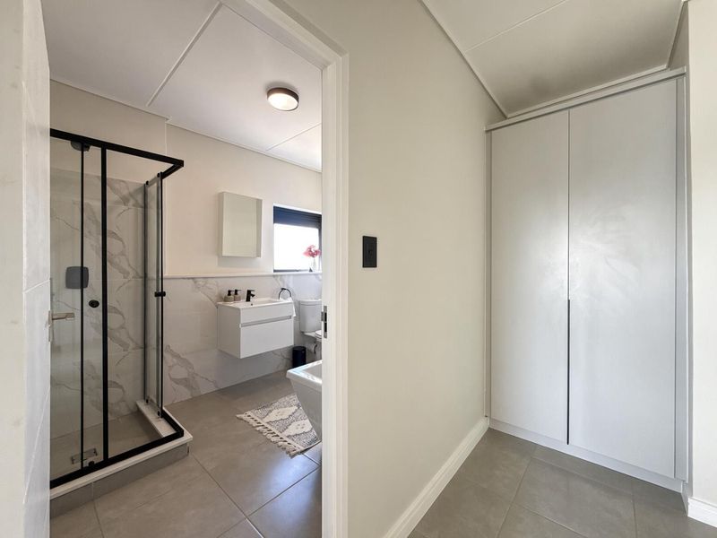 Modern bathroom featuring a walk-in shower with black frame, wall-mounted vanity, and adjacent built-in storage cupboard in a clean, neutral finish.