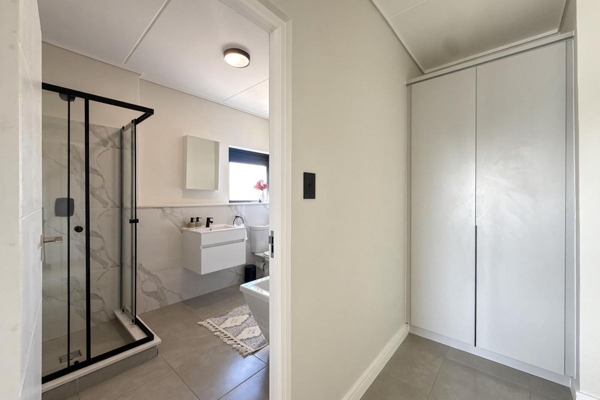 Modern bathroom featuring a walk-in shower with black frame, wall-mounted vanity, and adjacent built-in storage cupboard in a clean, neutral finish.