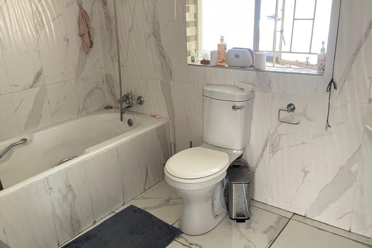 A functional bathroom featuring marble-look wall and floor tiling, a standard bathtub, and a pedestal basin.