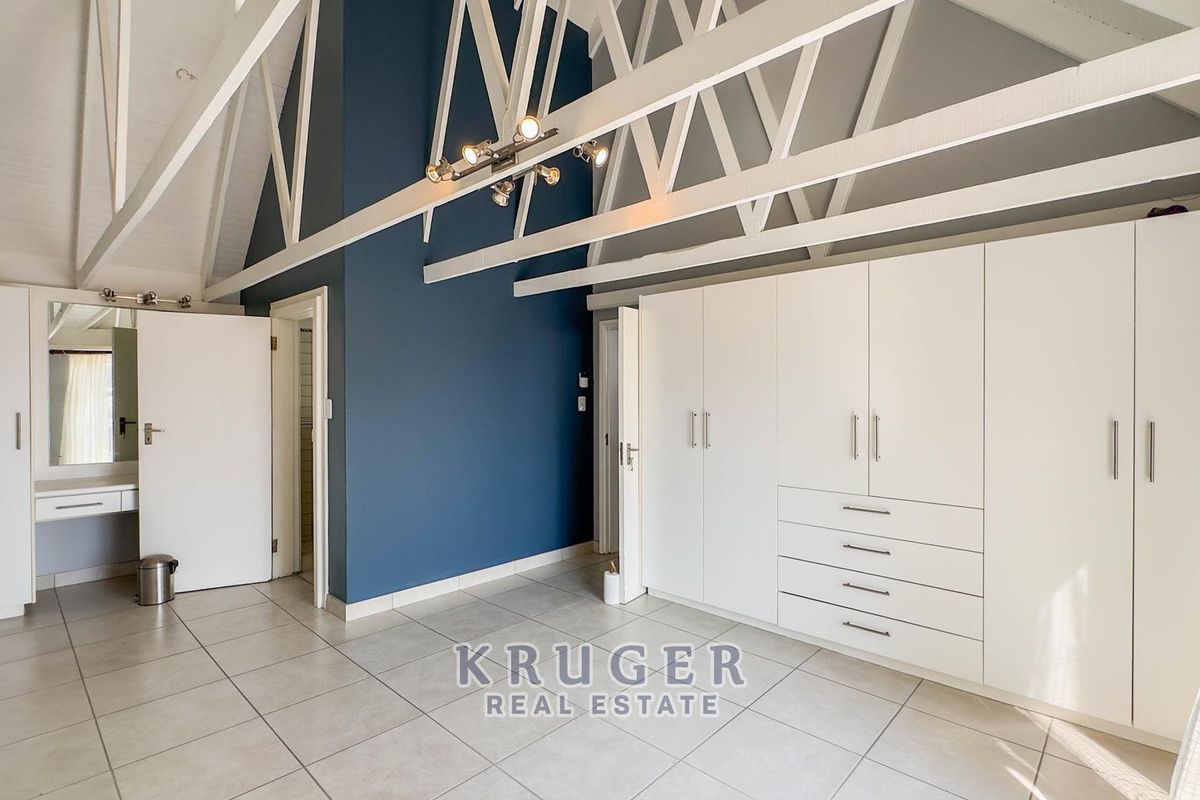 Spacious bedroom featuring high vaulted ceilings with exposed white trusses, extensive built-in cabinetry, tiled flooring, and a dedicated vanity area.