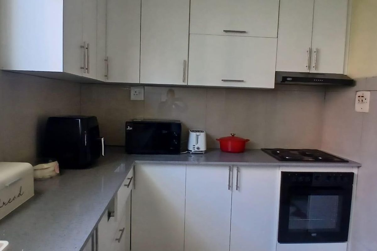 A functional kitchen featuring white cabinetry, stone countertops, a built-in oven, and an electric hob with an extractor fan.