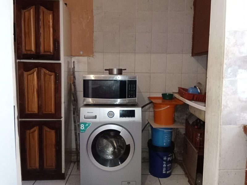 A small laundry area featuring built-in wooden cabinetry and tiled wall finishes, currently showing signs of wear and maintenance requirements.