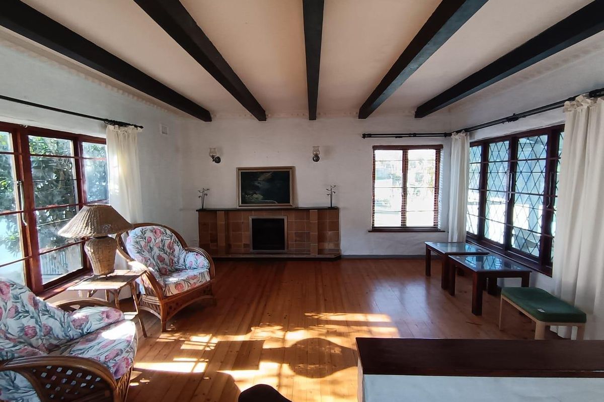 Spacious living room featuring exposed timber ceiling beams, polished timber flooring, a tiled fireplace, and large leaded glass windows providing ample natural light.