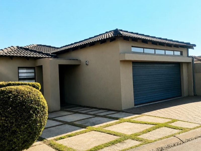 Front elevation of a modern house featuring a tiled roof, a secure roller garage door, and a paved driveway with integrated grass strips.