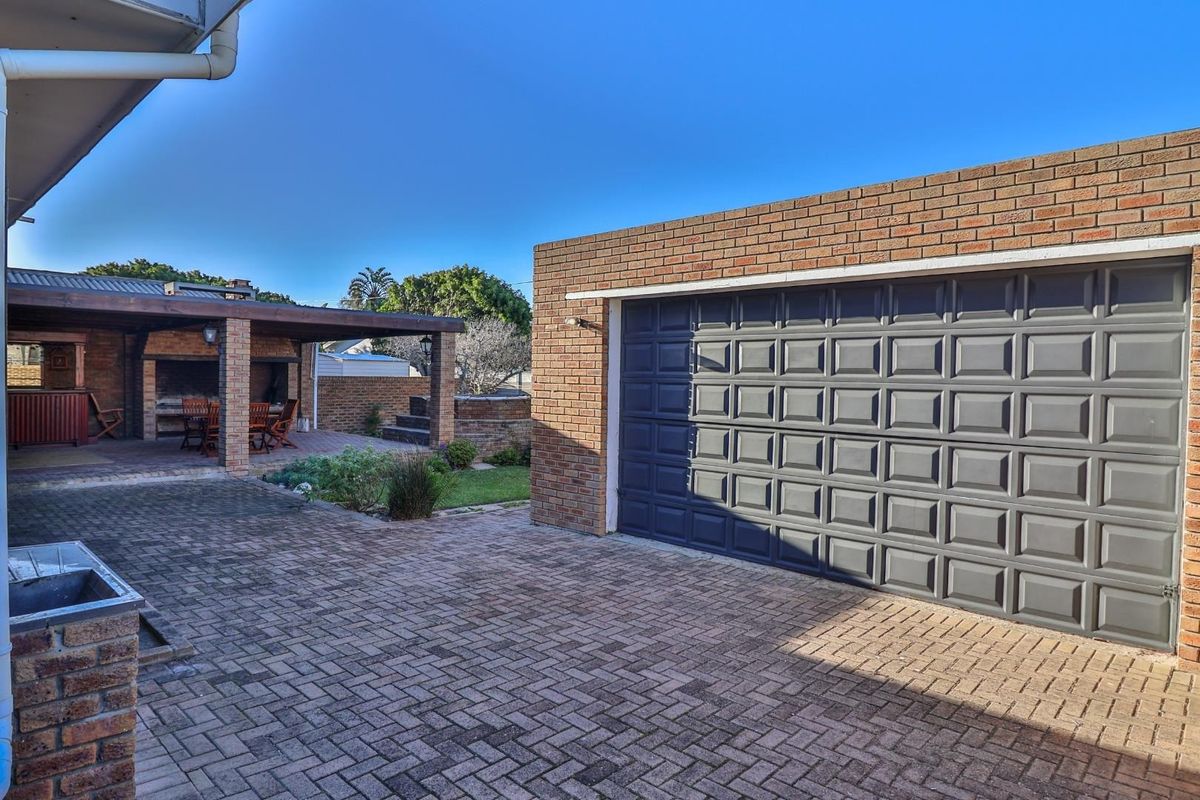 Rear exterior view featuring a paved courtyard, a covered patio area with built-in braai, and a detached brick garage.