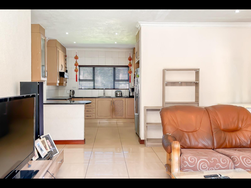Open-plan living and kitchen area featuring tiled flooring, neutral walls, and functional wooden cabinetry with granite countertops.