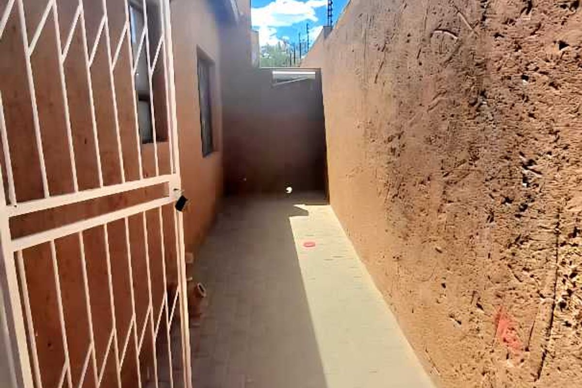 A narrow exterior side passage featuring paved flooring, a security gate, and high boundary walls with electric fencing.