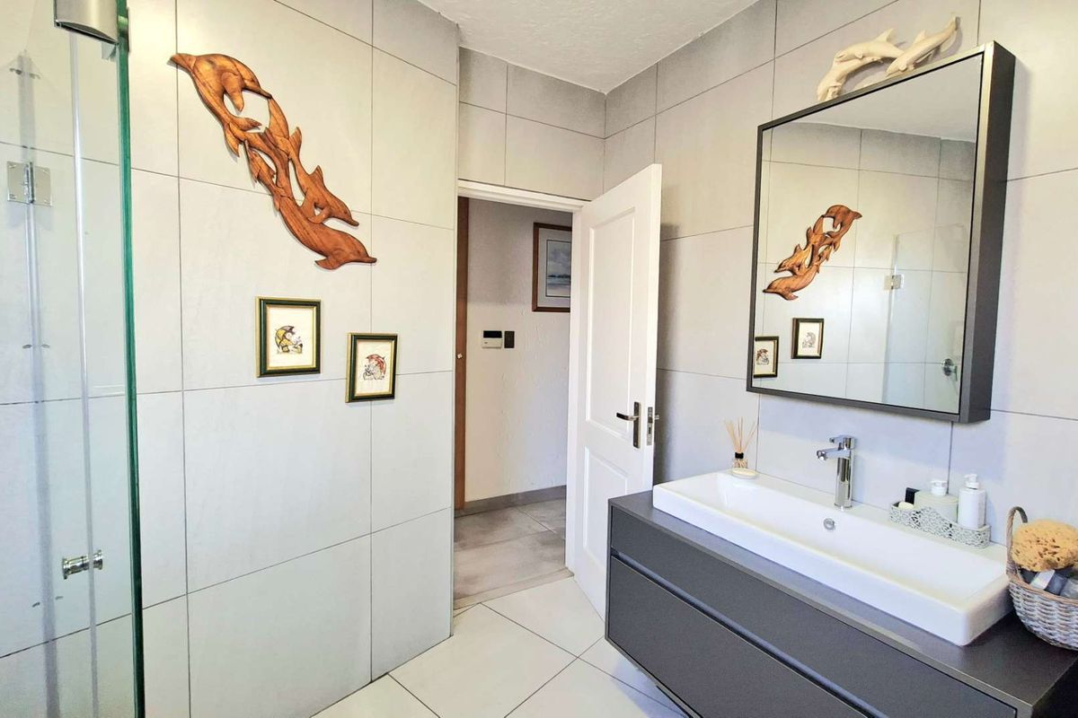 Modern bathroom featuring large format wall tiles, a floating vanity with a rectangular basin, a framed mirror, and a glass-enclosed shower.