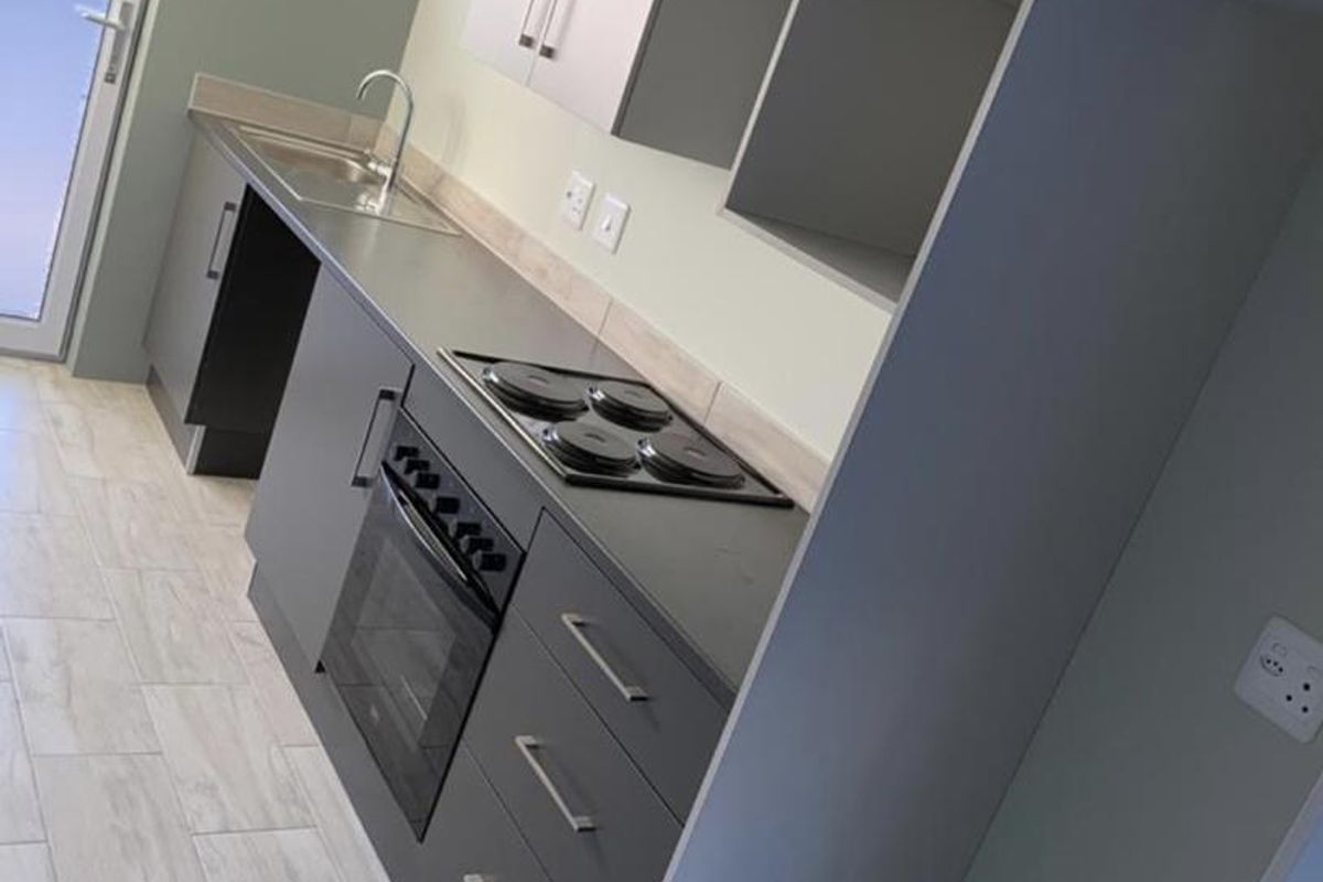 Modern kitchen featuring sleek grey cabinetry, built-in oven and hob, stainless steel sink, and light-toned tiled flooring with direct access to the exterior.