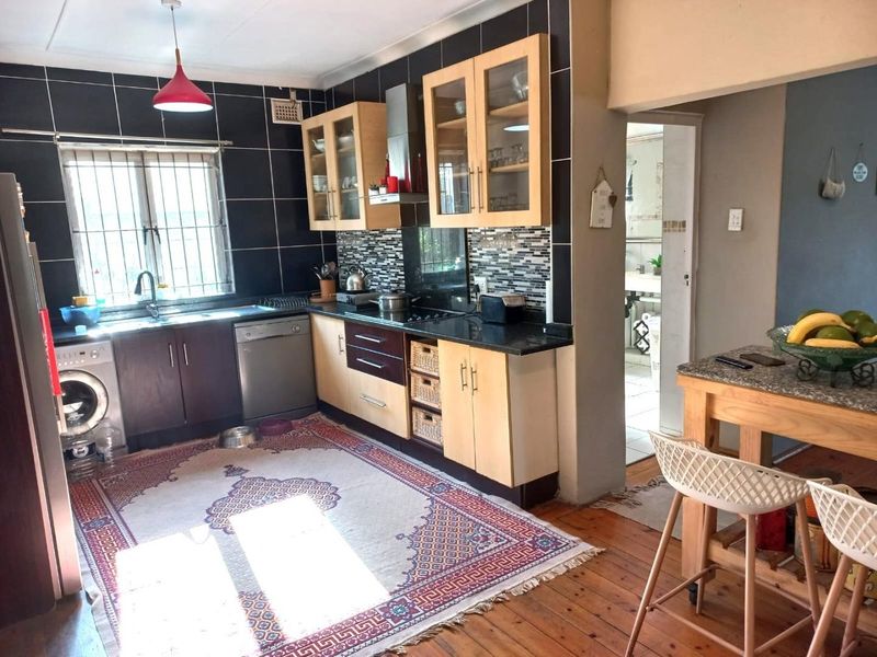 A functional kitchen featuring built-in cabinetry, granite countertops, a tiled backsplash, and integrated appliances, with direct access to an adjacent room.