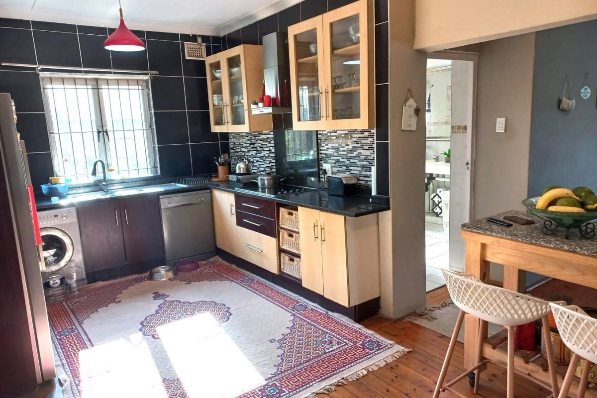 A functional kitchen featuring built-in cabinetry, granite countertops, a tiled backsplash, and integrated appliances, with direct access to an adjacent room.