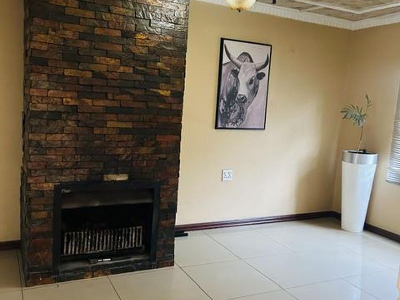 A living room featuring a prominent stone-clad fireplace, tiled flooring, and decorative ceiling detailing, offering a neutral space ready for personalization.
