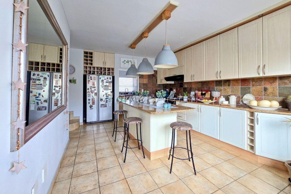 A functional kitchen featuring granite countertops, a central island with pendant lighting, ample built-in cabinetry, and a decorative tile backsplash.