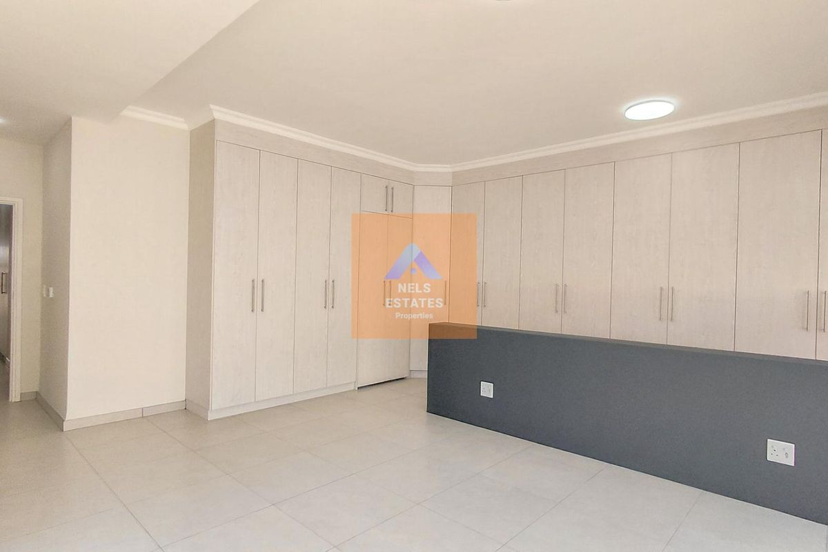 A spacious, empty bedroom featuring extensive built-in cupboards, neutral tiled flooring, and modern recessed ceiling lighting.
