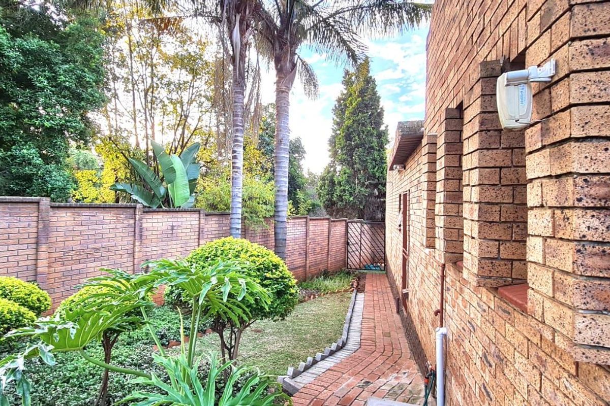 A side view of the property featuring face brick exterior walls, a paved walkway, and a well-maintained garden with a brick boundary wall.