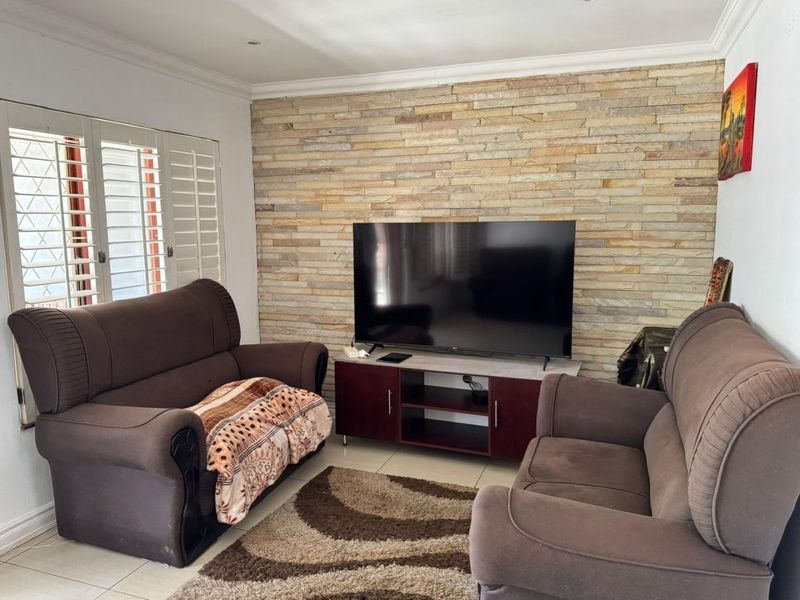 A comfortable living room featuring a textured stone accent wall, tiled flooring, and plantation shutters, providing a neutral base for interior design.