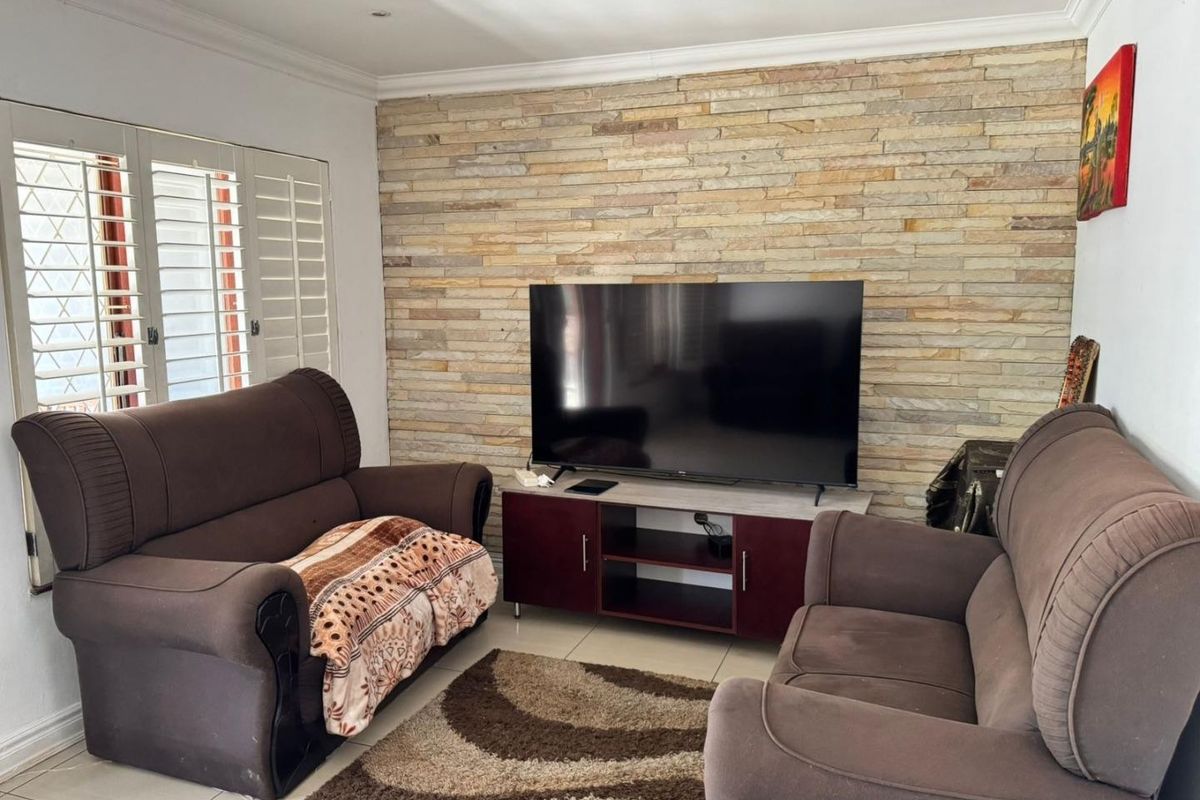 A comfortable living room featuring a textured stone accent wall, tiled flooring, and plantation shutters, providing a neutral base for interior design.