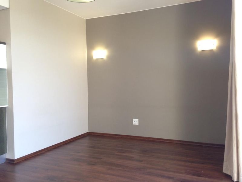 An empty living room featuring dark laminate flooring, neutral painted walls, and modern wall-mounted lighting fixtures.