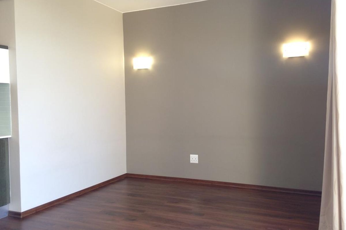 An empty living room featuring dark laminate flooring, neutral painted walls, and modern wall-mounted lighting fixtures.