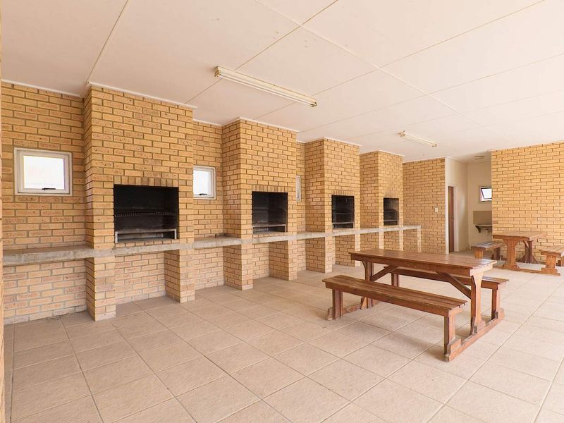 A covered outdoor entertainment area featuring multiple built-in brick braais, concrete prep counters, and tiled flooring, suitable for communal gatherings.