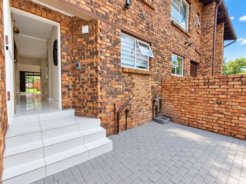 A well-maintained townhouse entrance featuring a face brick facade, paved driveway, and tiled steps leading into a bright, tiled interior hallway.