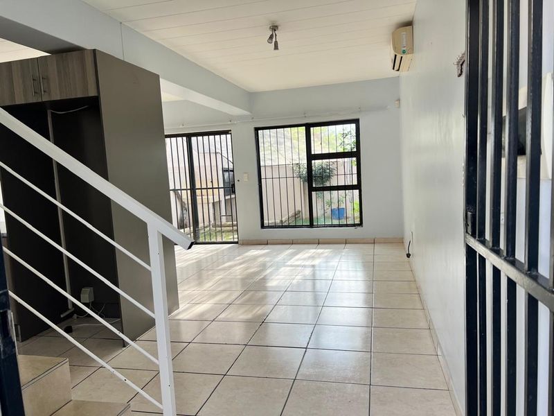 An open-plan living area featuring tiled floors, a staircase, and sliding doors with security bars, providing access to the exterior.