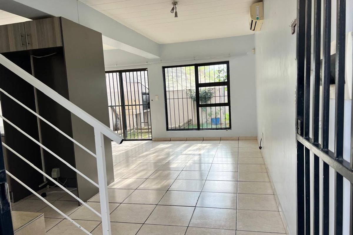 An open-plan living area featuring tiled floors, a staircase, and sliding doors with security bars, providing access to the exterior.