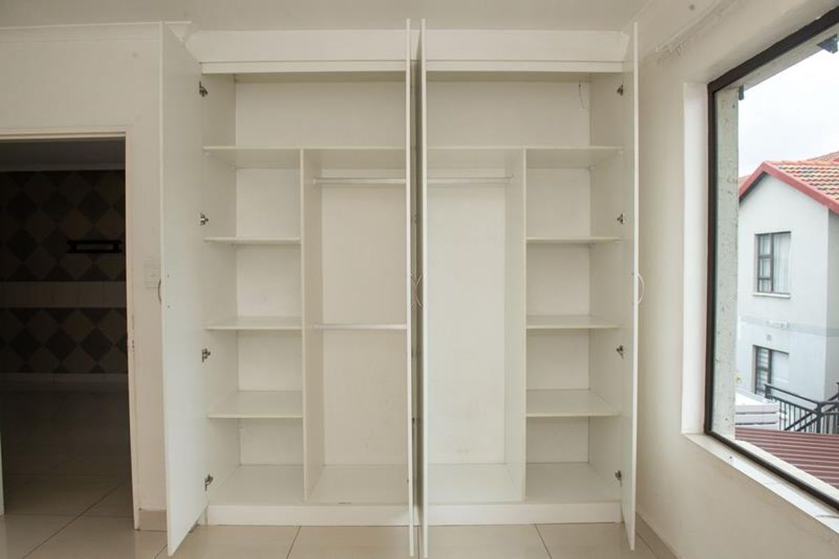 A bedroom featuring built-in white cabinetry with shelving and hanging rails, tiled flooring, and large windows providing natural light.