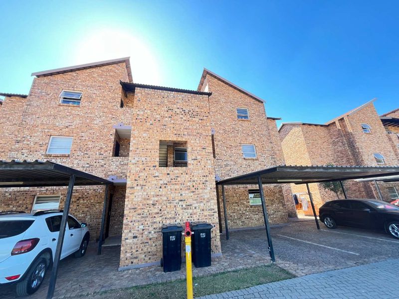 Exterior view of a multi-story face brick apartment building featuring covered parking bays and a paved driveway area.