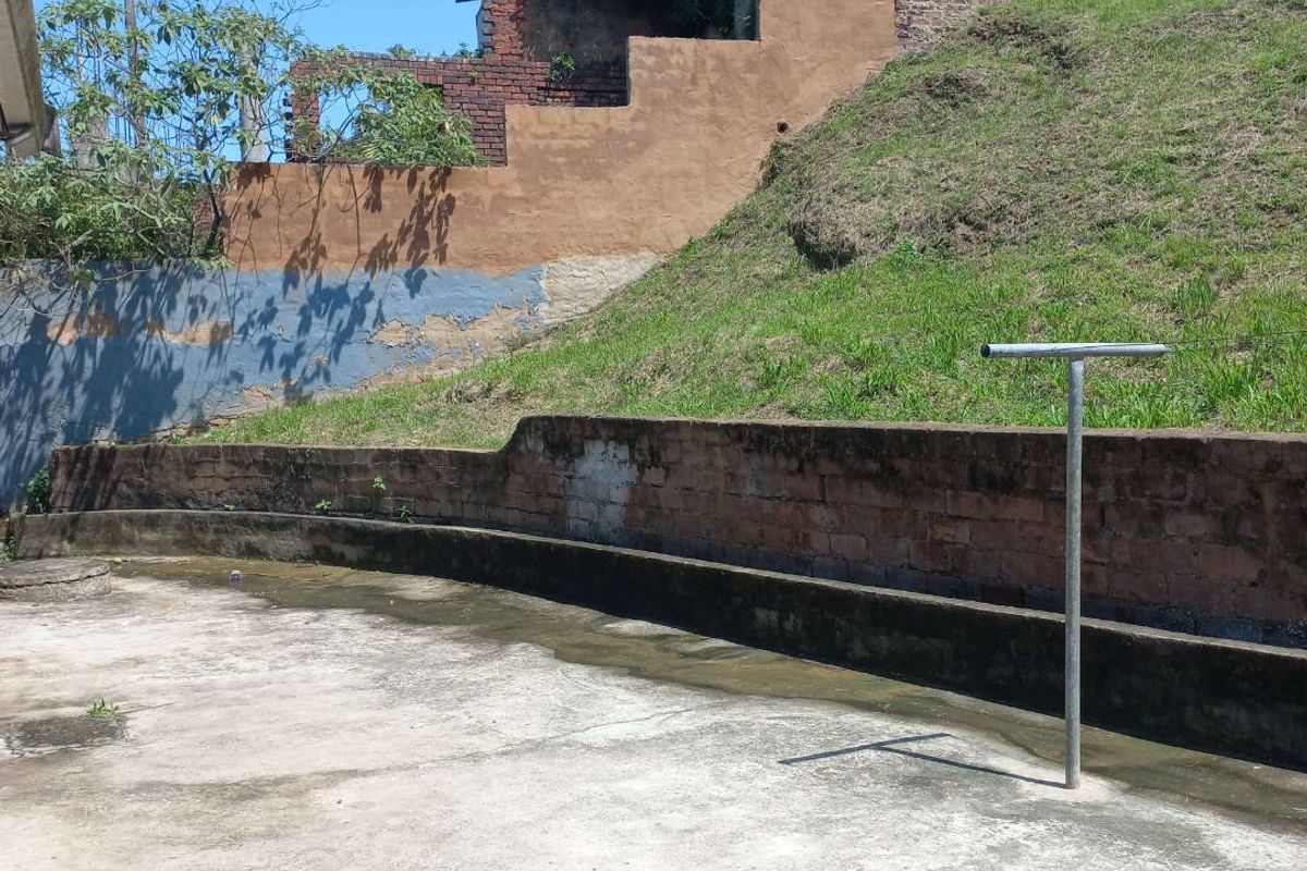 A rear outdoor area featuring a concrete patio, tiered retaining walls, and a sloped grass embankment, showing signs of significant weathering and wear.