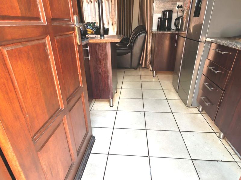 A compact kitchen featuring dark wood cabinetry, granite countertops, and light-colored ceramic floor tiles, with an integrated breakfast bar area.