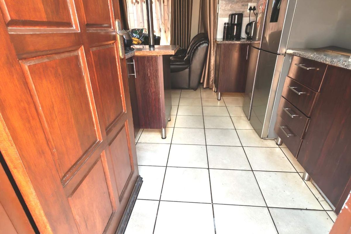A compact kitchen featuring dark wood cabinetry, granite countertops, and light-colored ceramic floor tiles, with an integrated breakfast bar area.