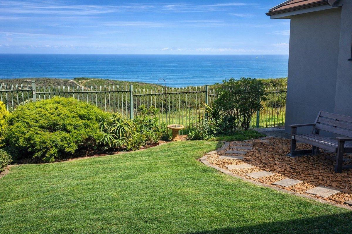 A well-maintained rear garden featuring a manicured lawn, stone pathway, and metal perimeter fencing, offering expansive ocean views.