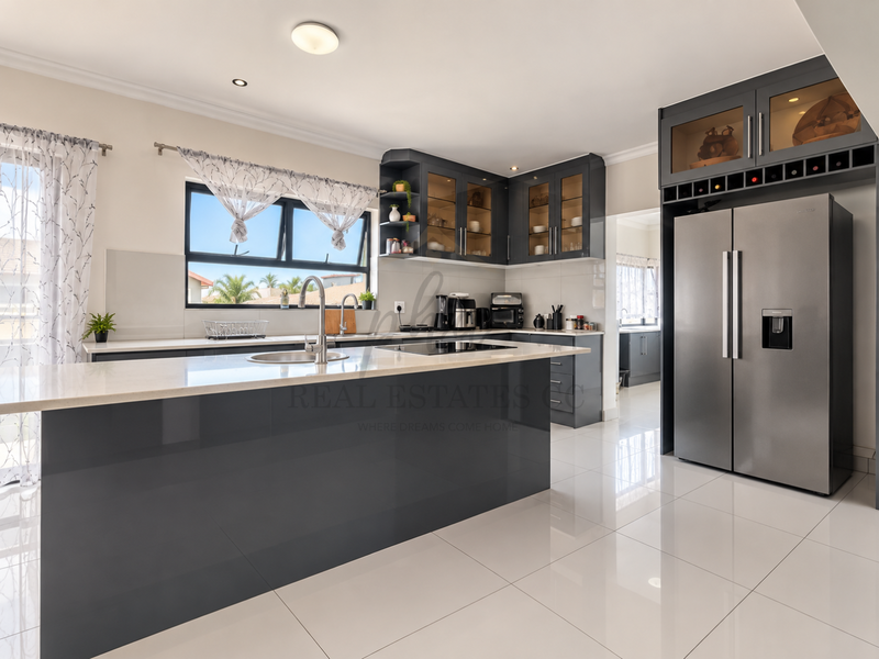 Modern kitchen featuring a large island with quartz countertops, sleek dark cabinetry, integrated appliances, and polished porcelain floor tiles.