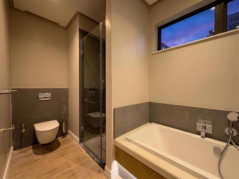 Modern bathroom featuring a wall-hung toilet, glass-enclosed shower, and a built-in bathtub with contemporary chrome fixtures and neutral tiling.