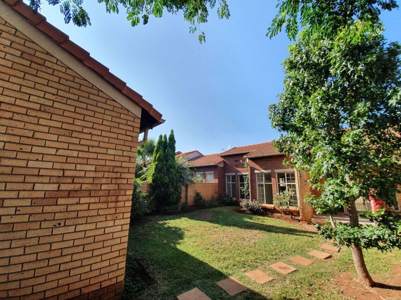 A private rear garden area featuring a well-maintained lawn, brick boundary walls, and established trees, providing a peaceful outdoor space for the townhouse.