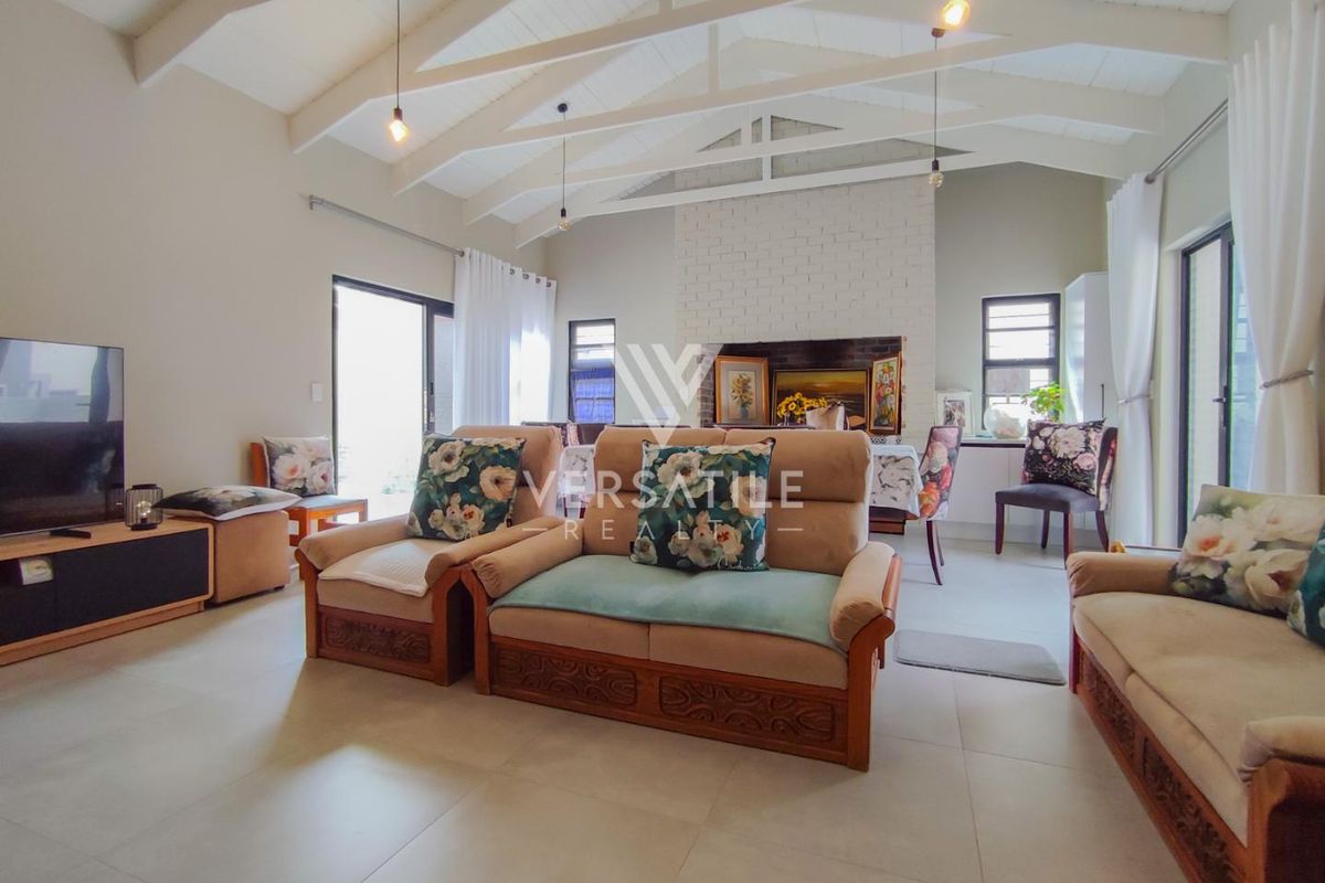 Spacious living room featuring a vaulted ceiling with exposed beams, tiled flooring, and a prominent brick fireplace, offering a bright and open atmosphere.