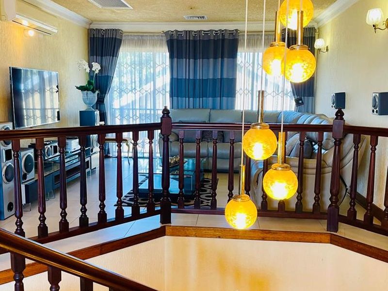Spacious living area featuring a wooden staircase balustrade, decorative pendant lighting, and split-system air conditioning, overlooking the lower level.