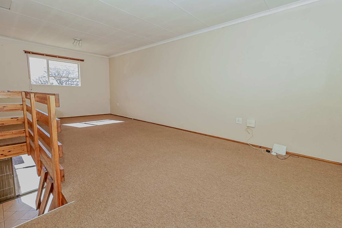 An empty, carpeted living area featuring a wooden staircase and neutral walls, offering a blank canvas for interior design.