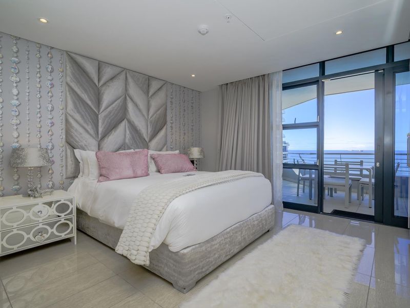 Modern bedroom featuring a large upholstered headboard, tiled flooring, and direct access to a private balcony with ocean views.